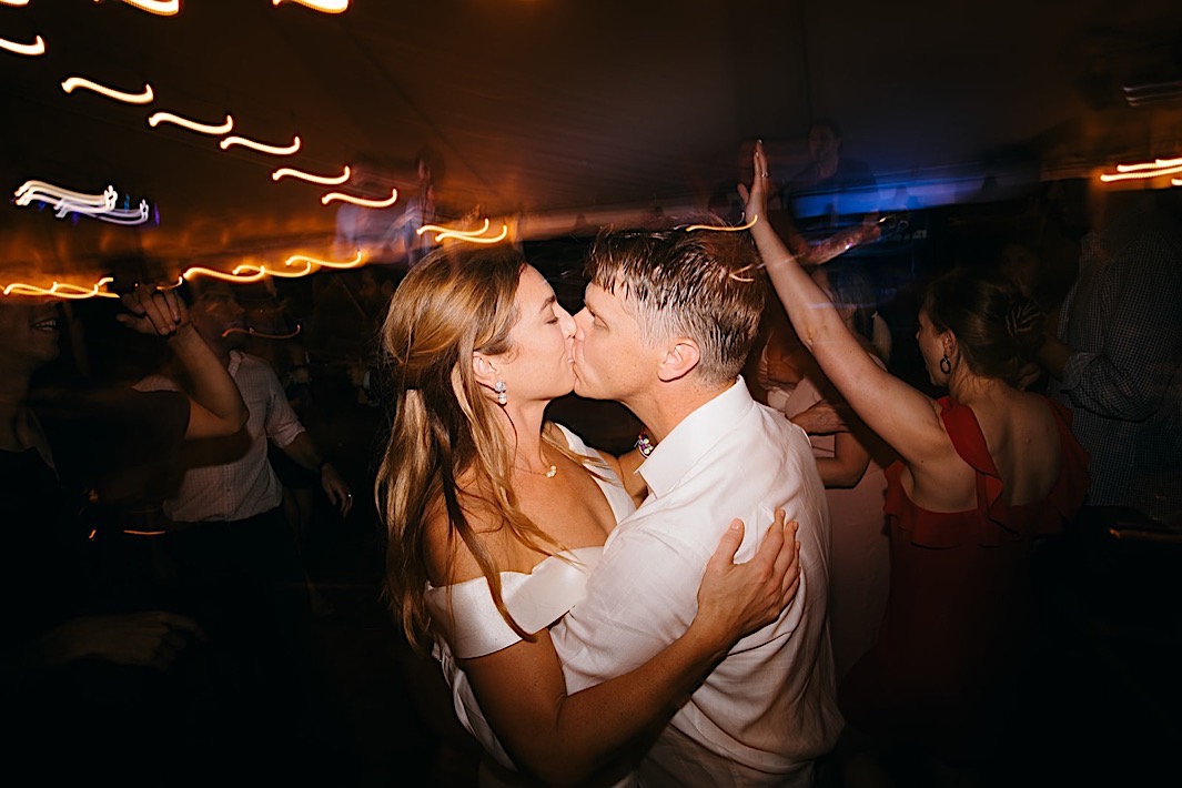 A bride and groom kiss on a crowded dancefloor.