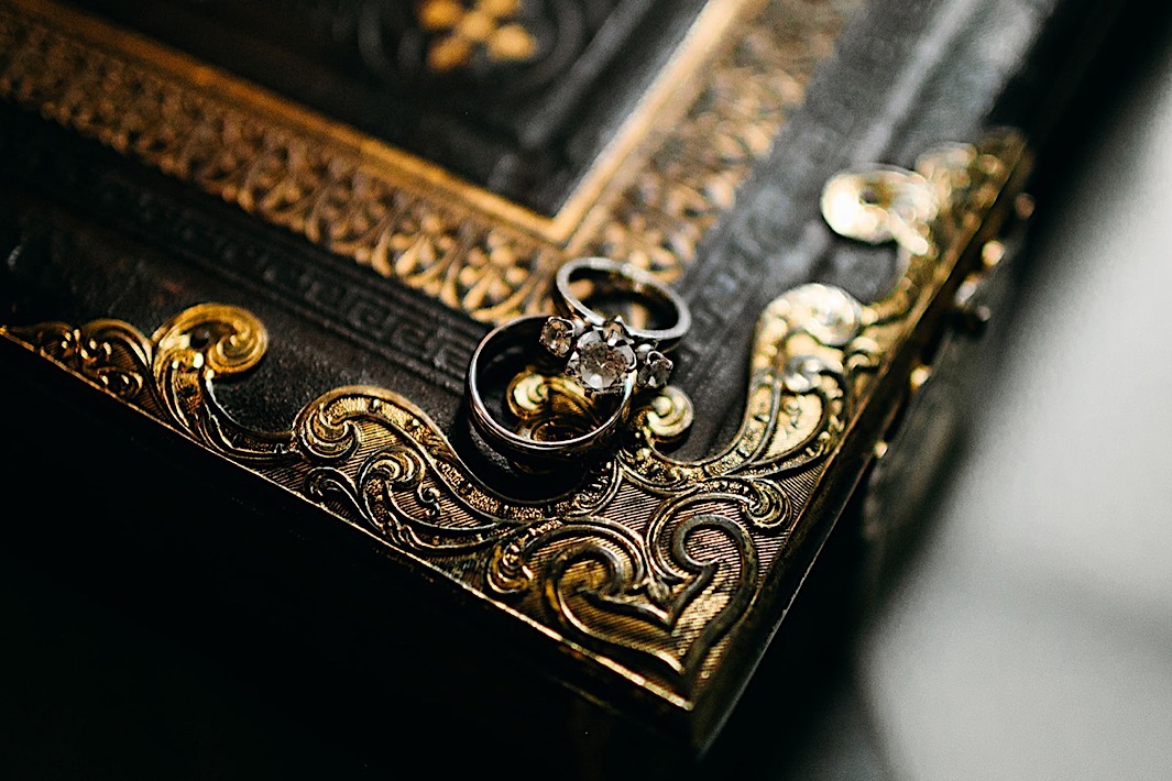 An engagement ring and wedding band balanced on the cover of an antique black and gold book.