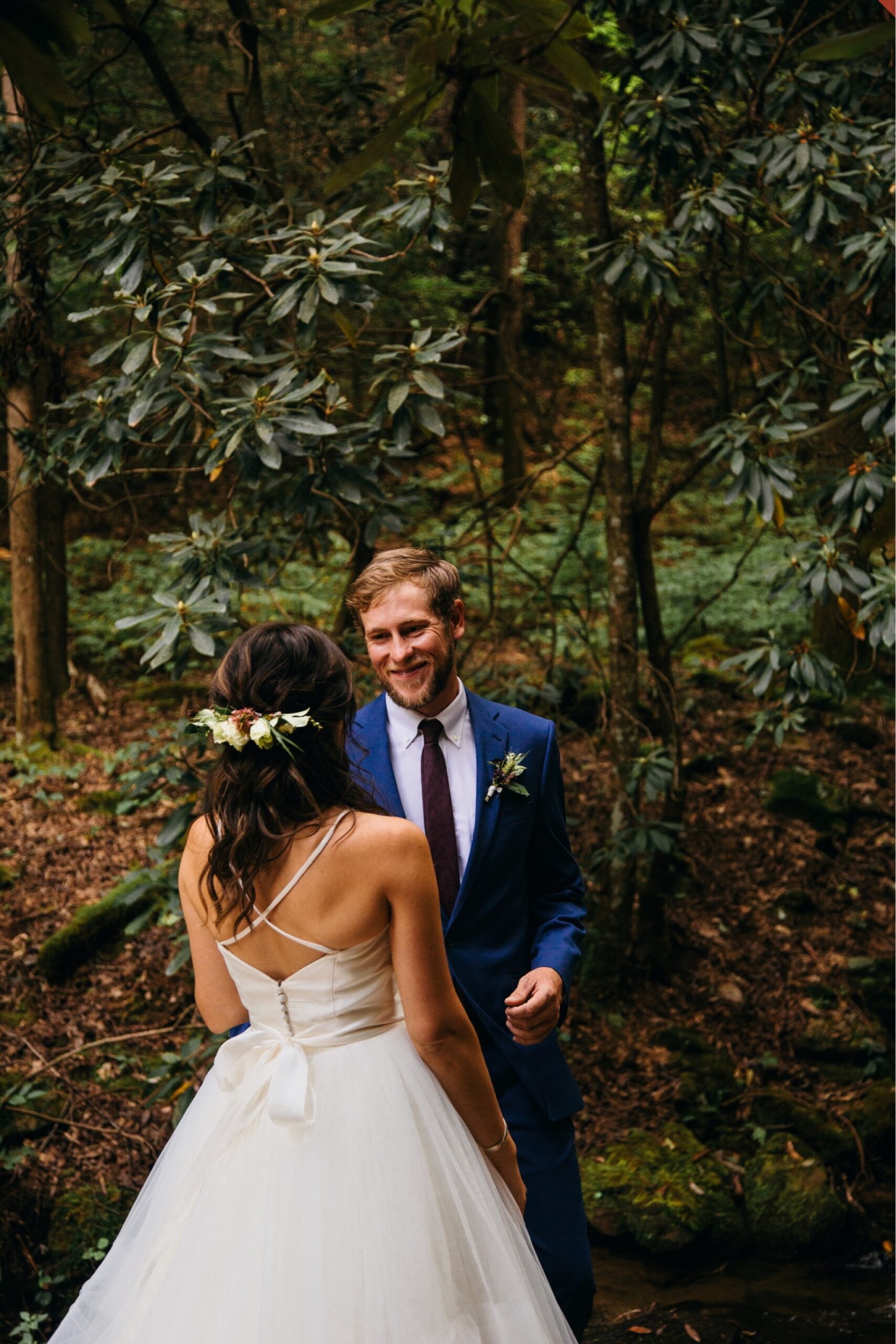The bride and groom smile at one another during their first look in the forest.