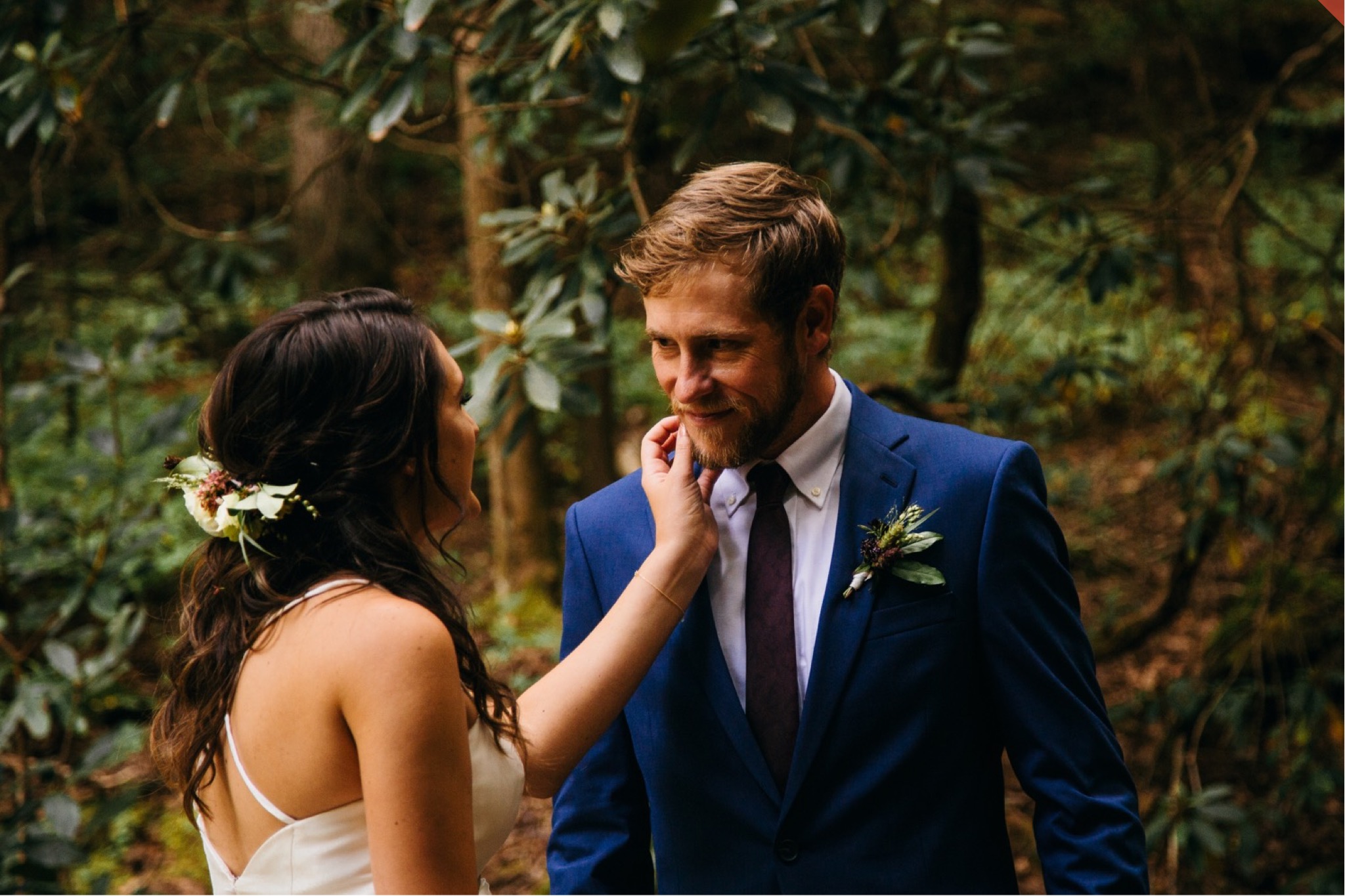 The bride strokes the groom's beard during their first look in the woods.