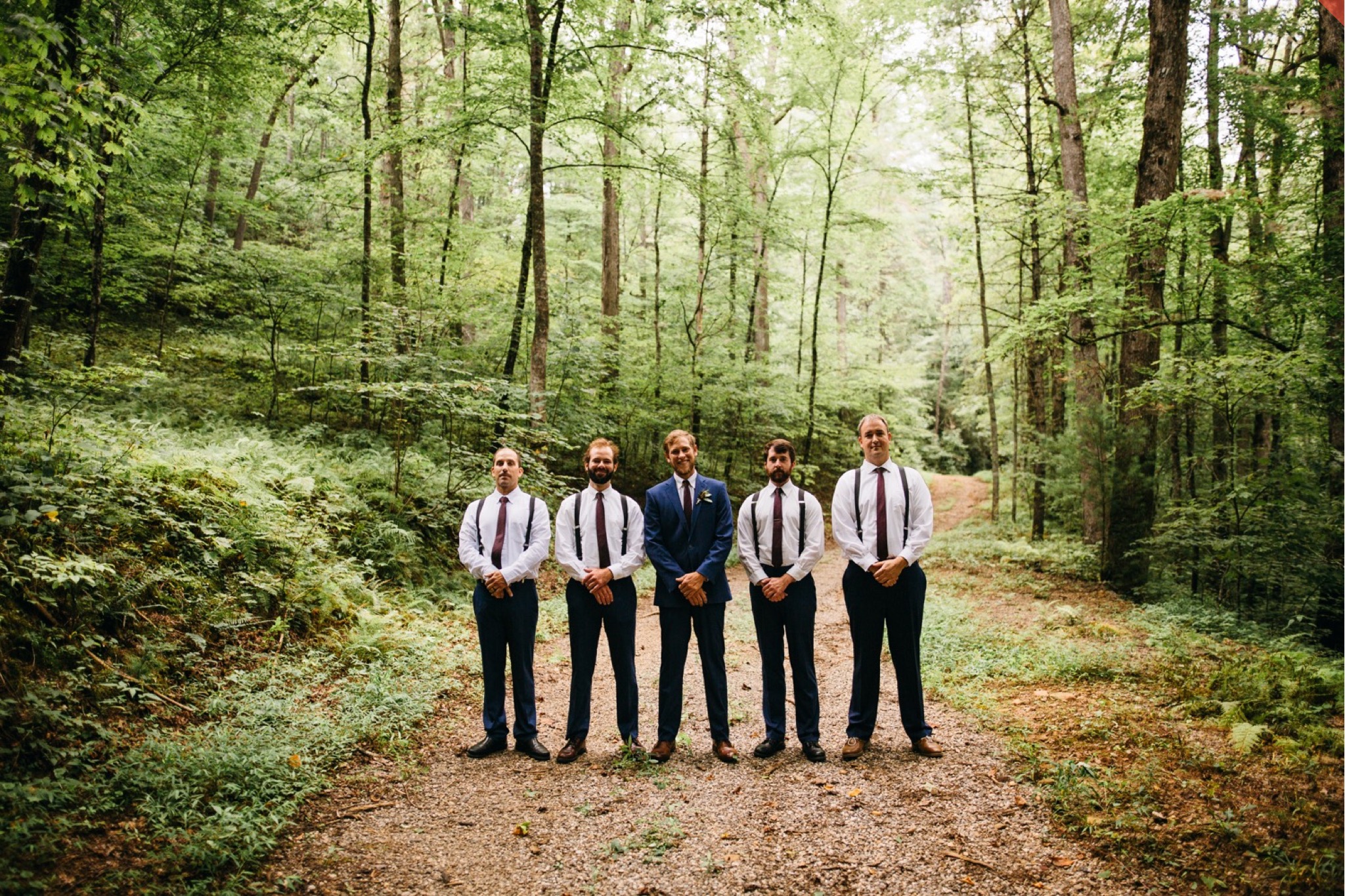 The groom poses on a forest path with his four groomsmen.