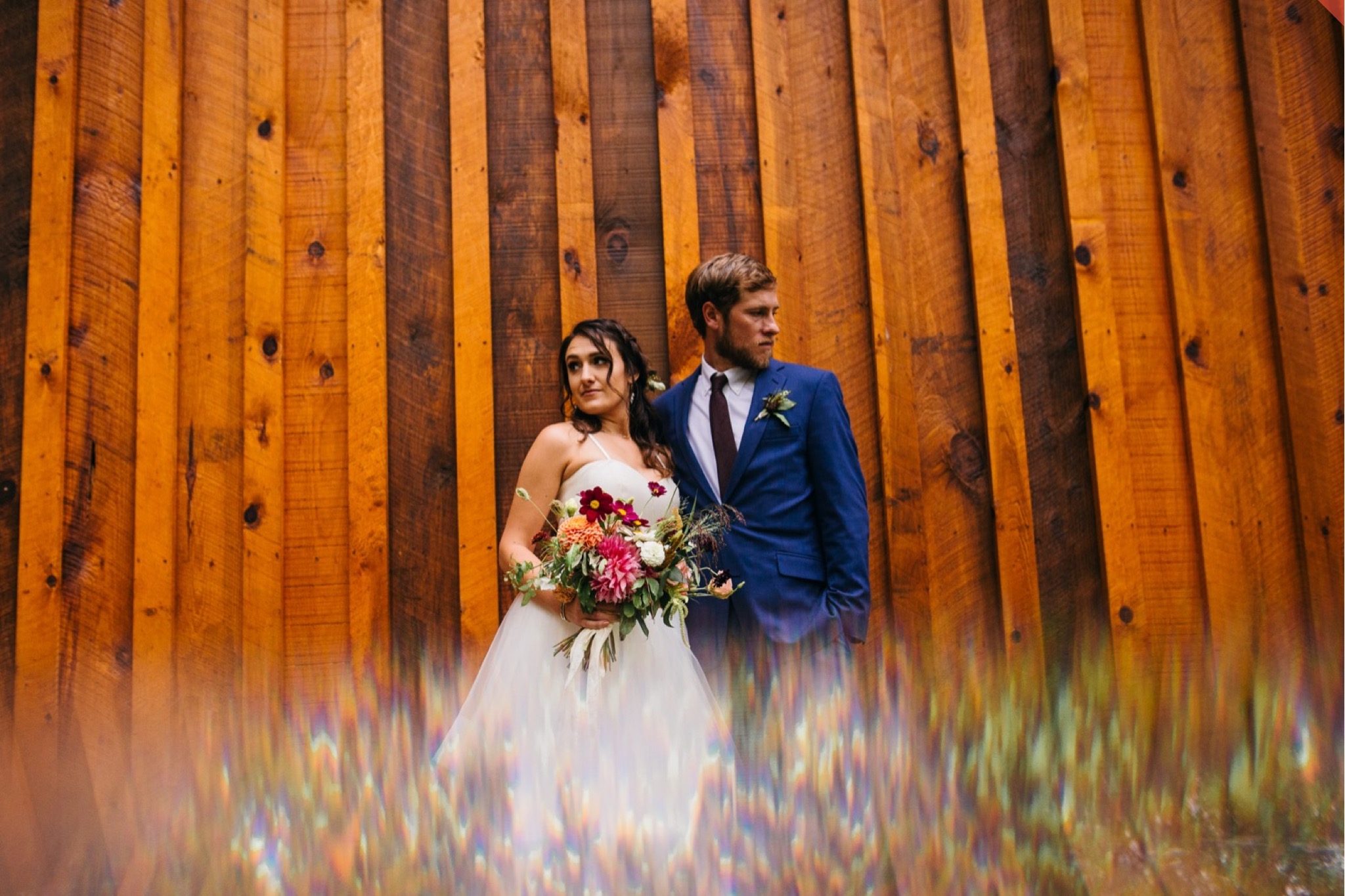 The bride and groom stand together looking in opposite directions against a wood paneled wall.