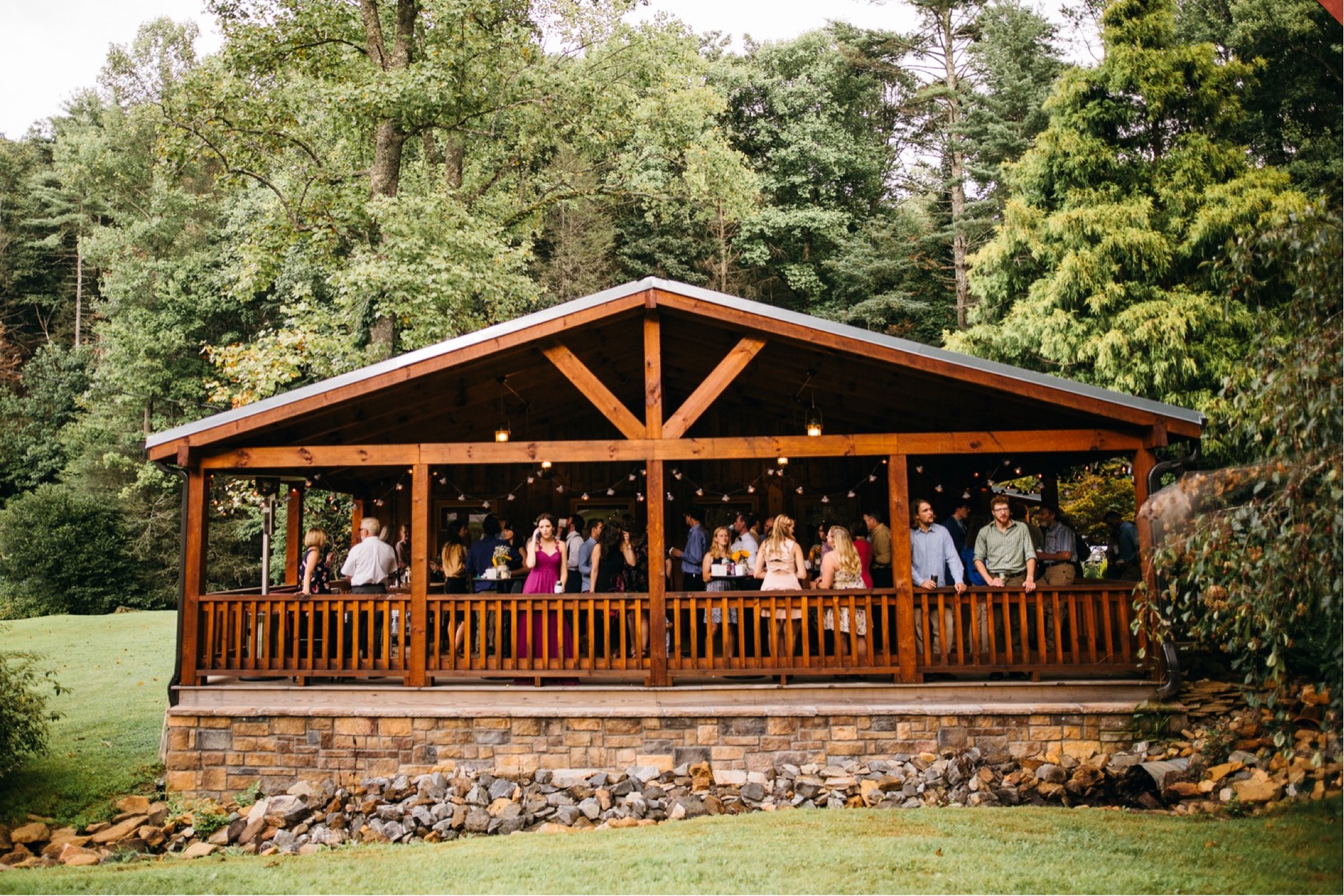 Wedding guests enjoy cocktail hour on a covered patio in the woods.