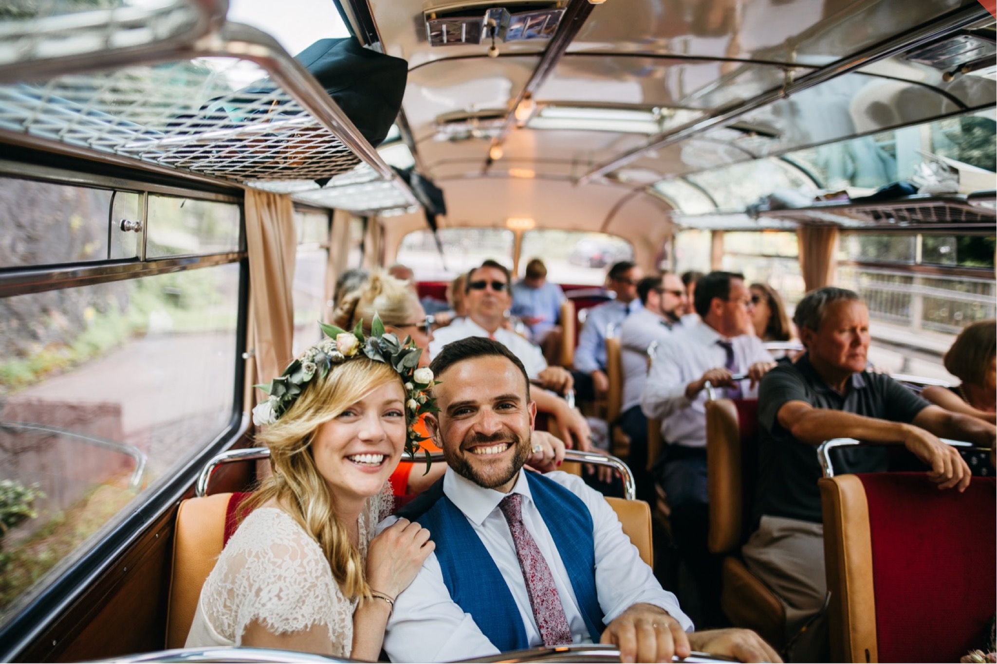 Bride and groom sit together with their guests on a vintage bus.