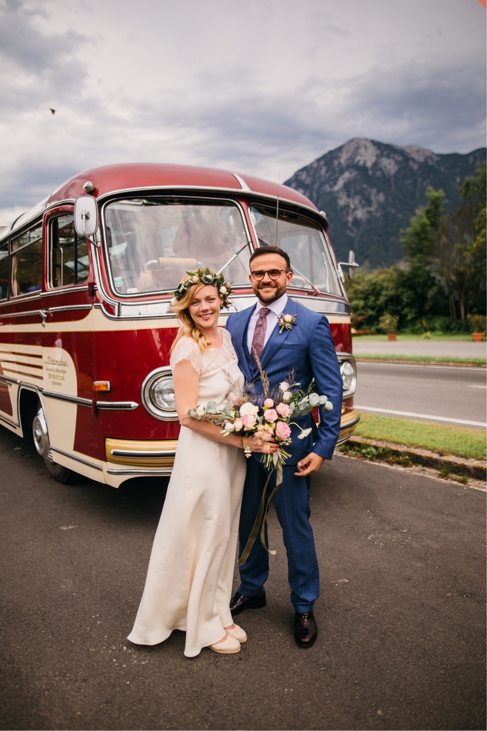 Bridge and groom pose together in front of a vintage bus.