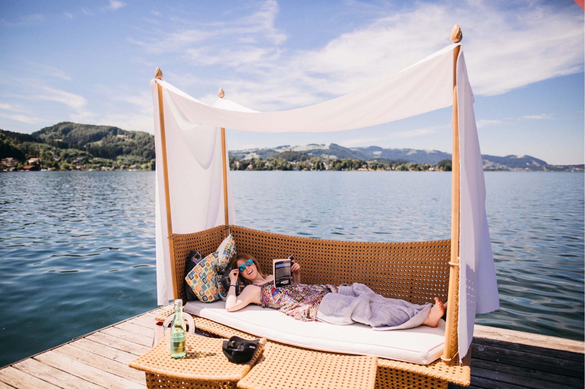 A woman lounges on a chaise on a dock atop an Austrian lake.