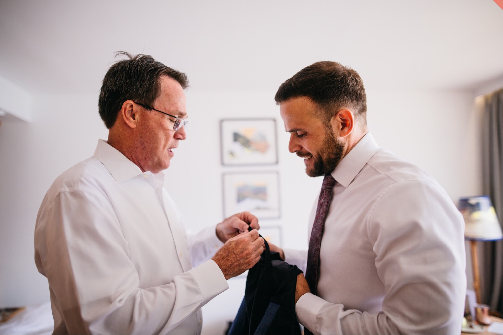 The groom gets help with his suit jacket as he gets ready for the wedding.