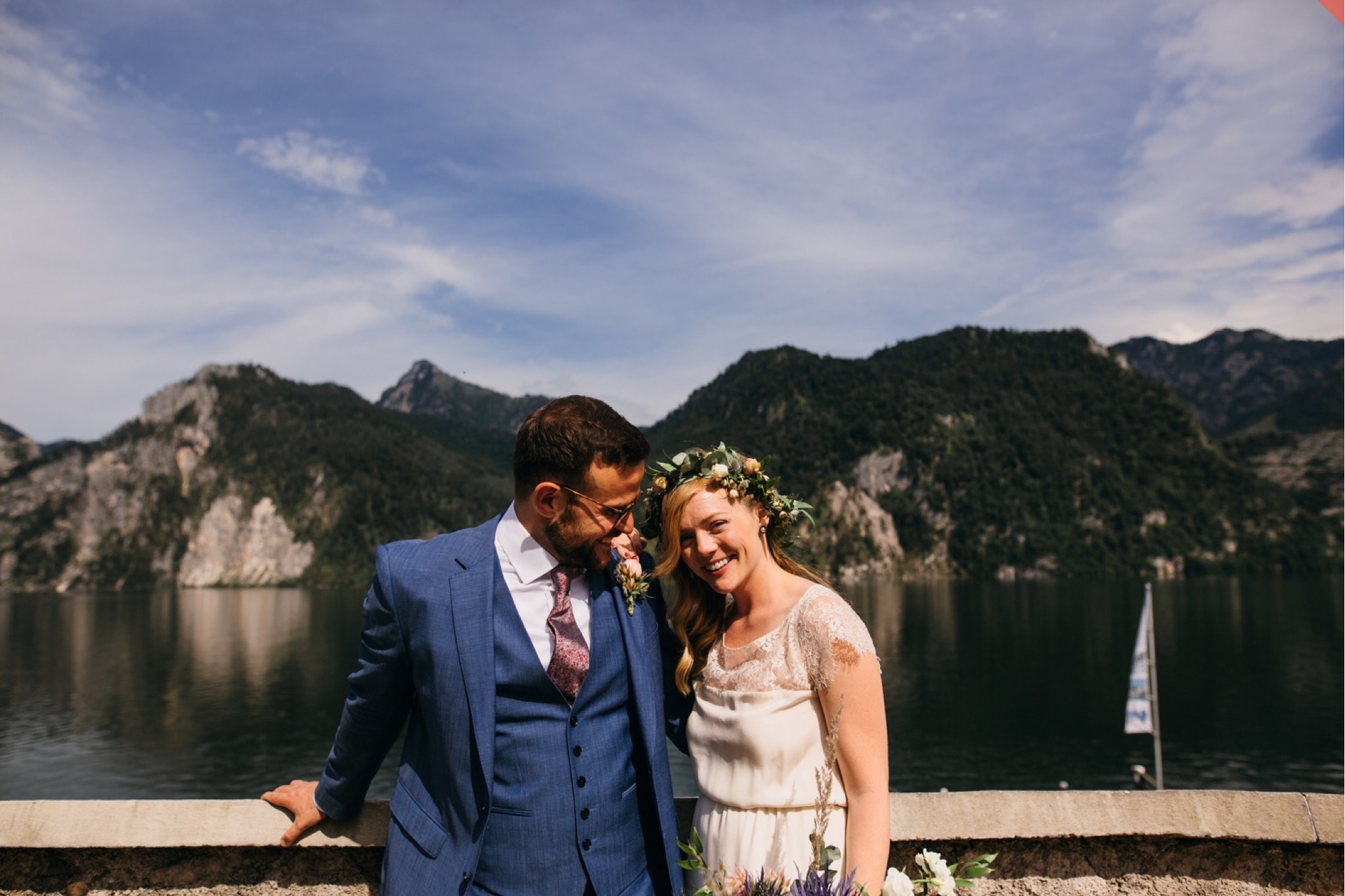 Bride and groom laugh together in front of an alpine lake.
