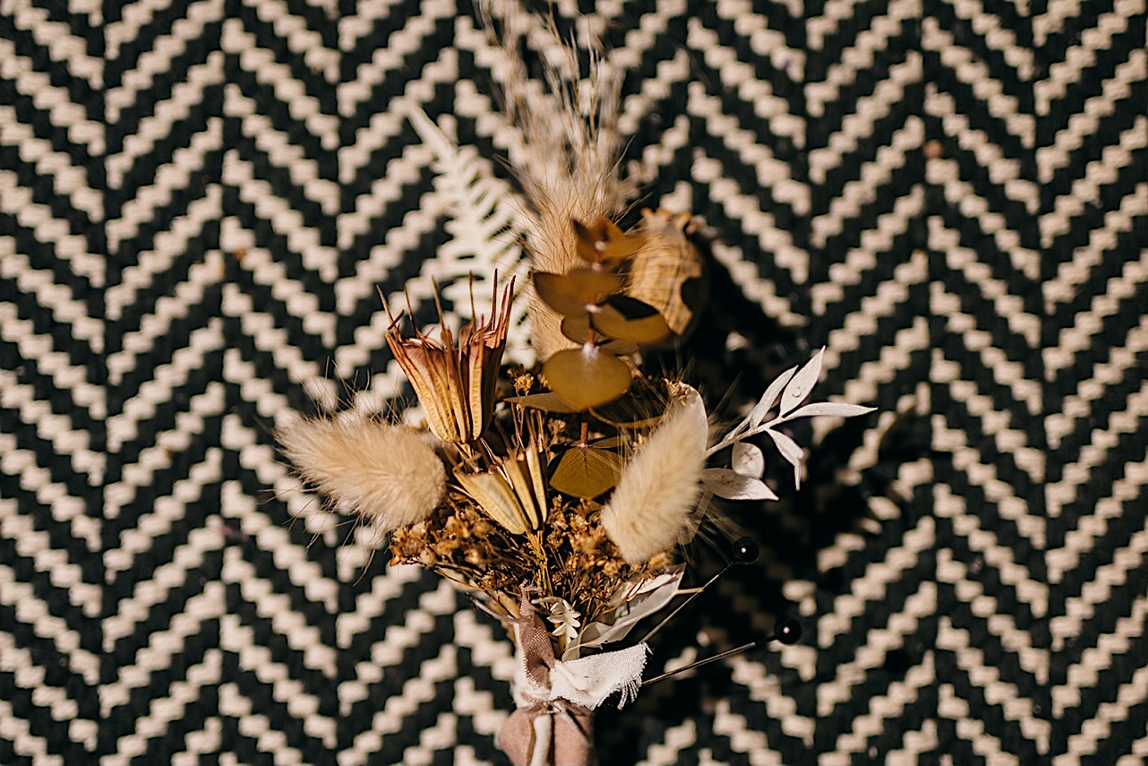 A boutonnière of dried flowers and grasses lying on a black and white rug.