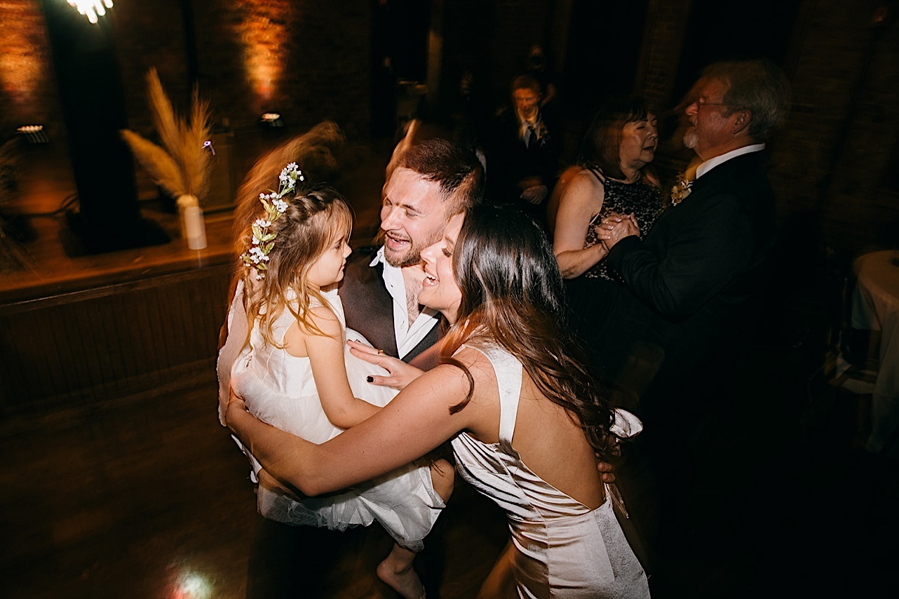 The bride and groom dance with the flower girl under party lights.