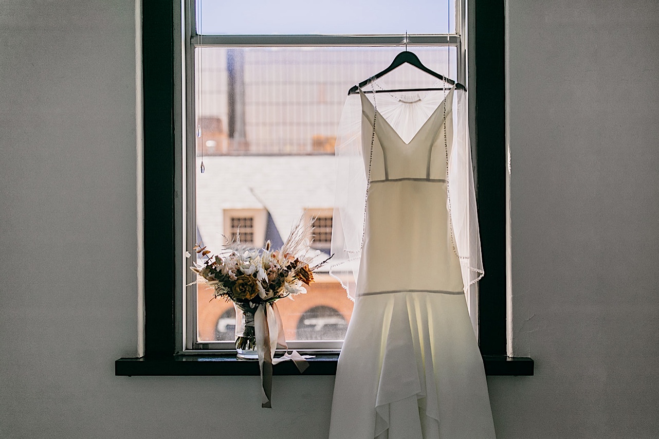 A bridal gown and bouquet resting in an open window.