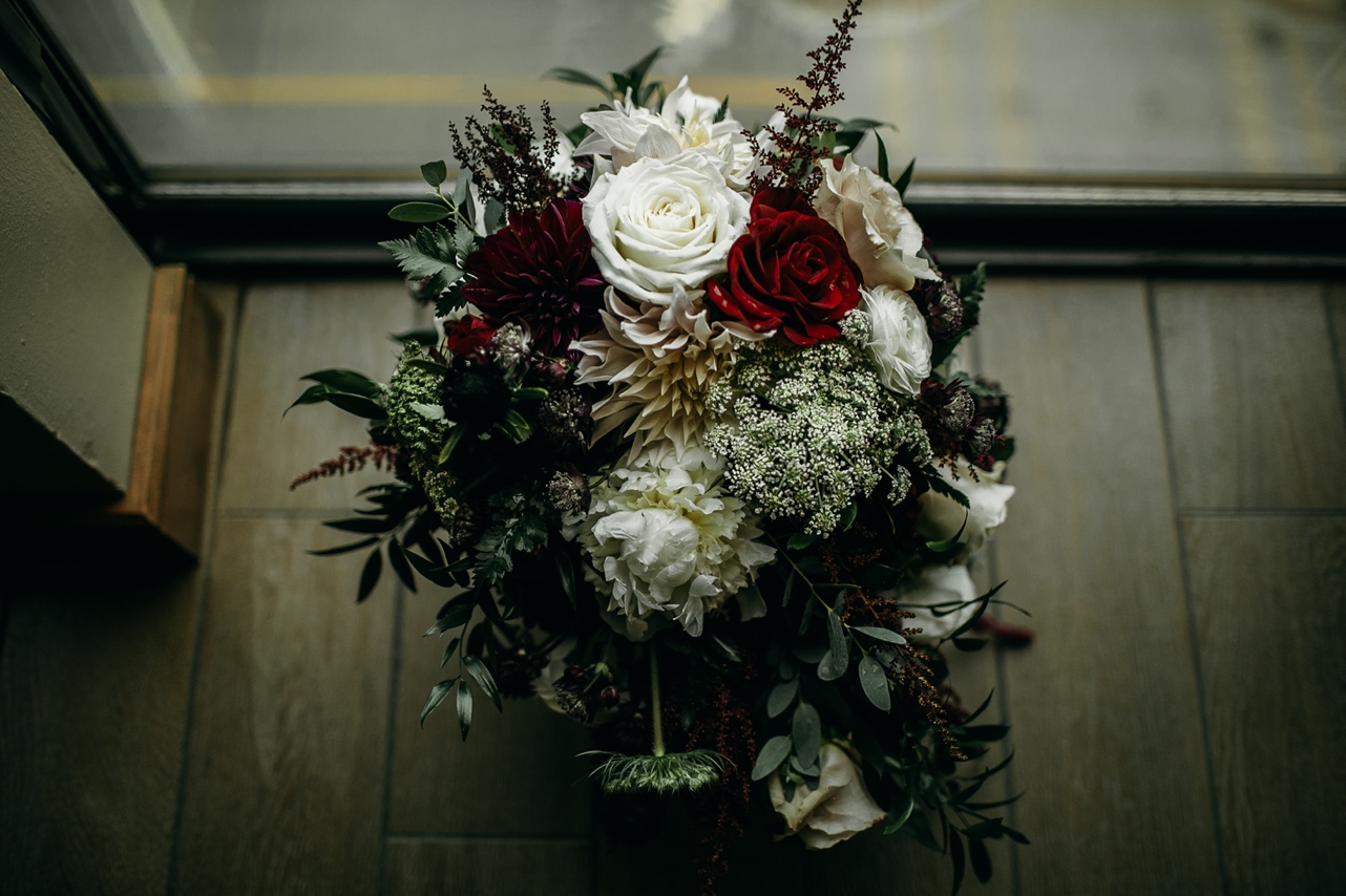 A bouquet of dark greens, burgundy, and white in a window.