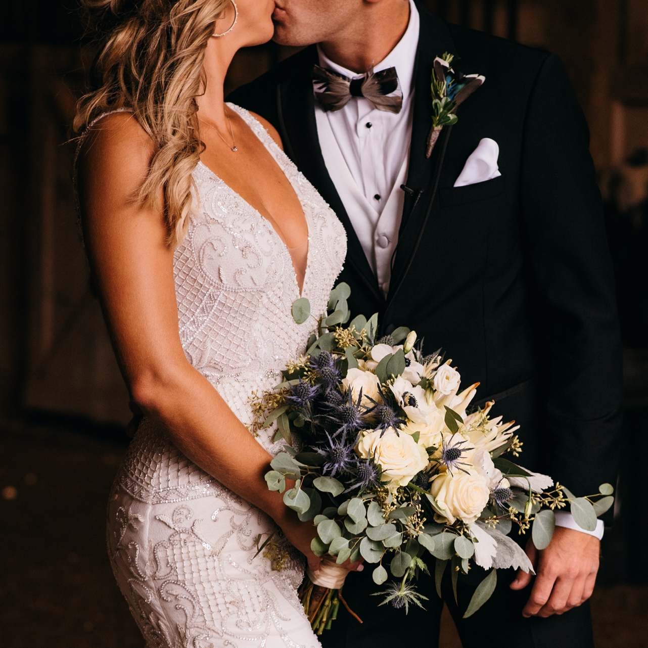 Bride and groom kiss while she holds her lush bouquet.