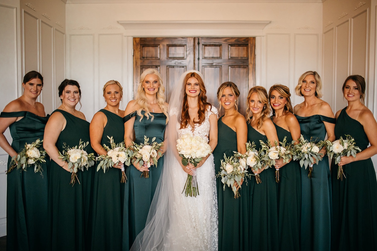 Bride poses with her bridesmaids, who are all wearing dark green dresses.
