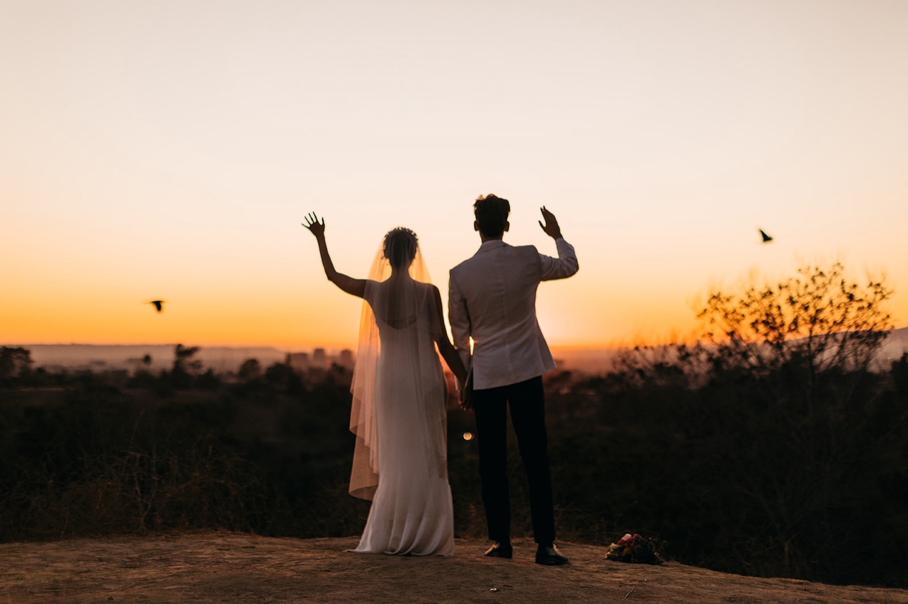 Bride and groom wave at birds flying by at sunset.