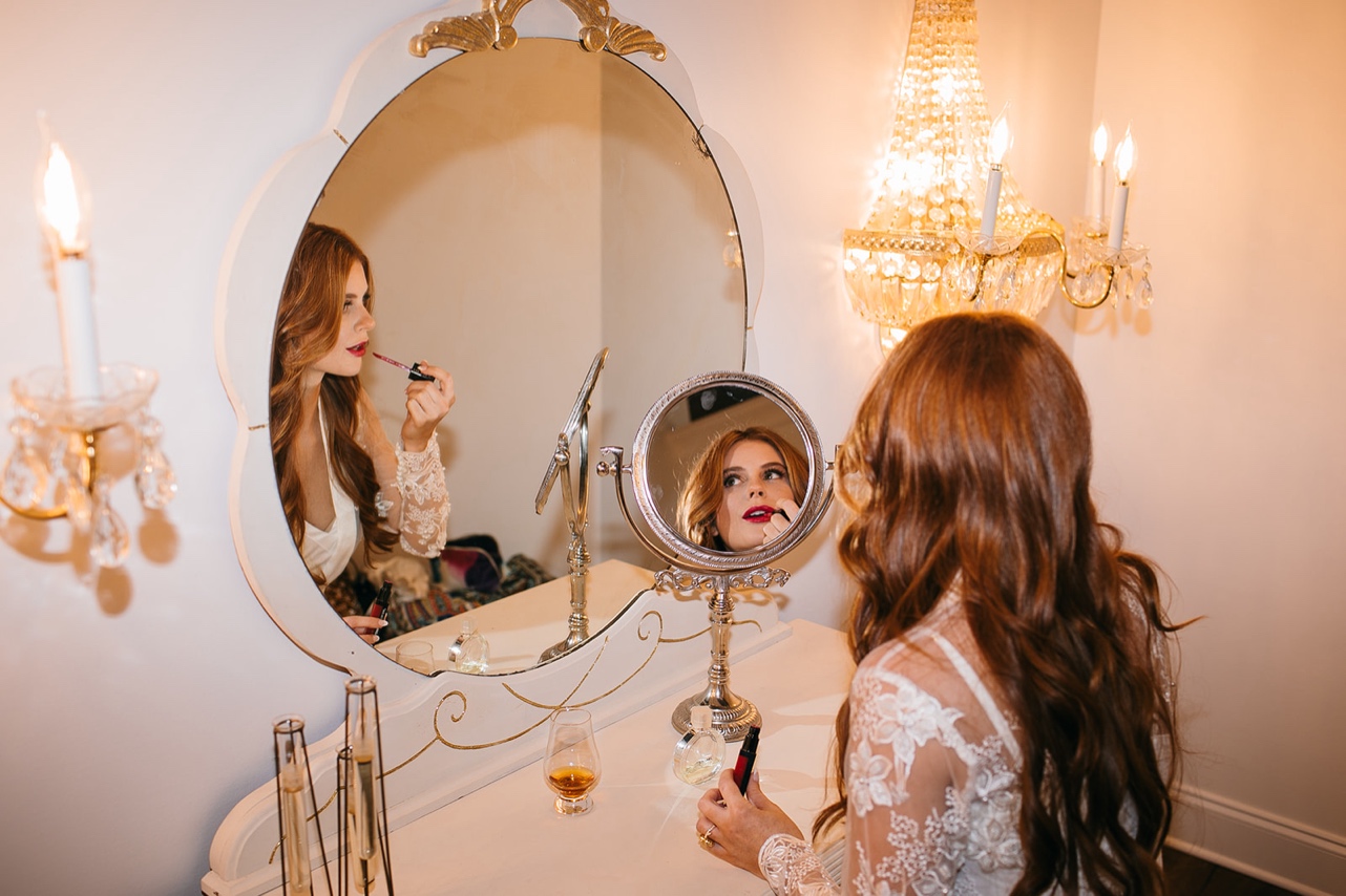 The bride applies her lipstick in a mirror.
