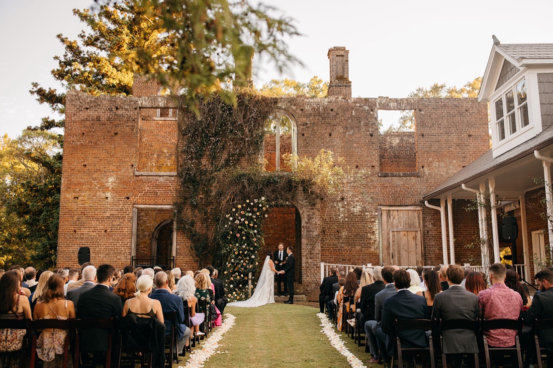 Barnsley Resort wedding photographer capture the exchange of vows in the ruins, surround by loved ones against a brick and vine backdrop. 