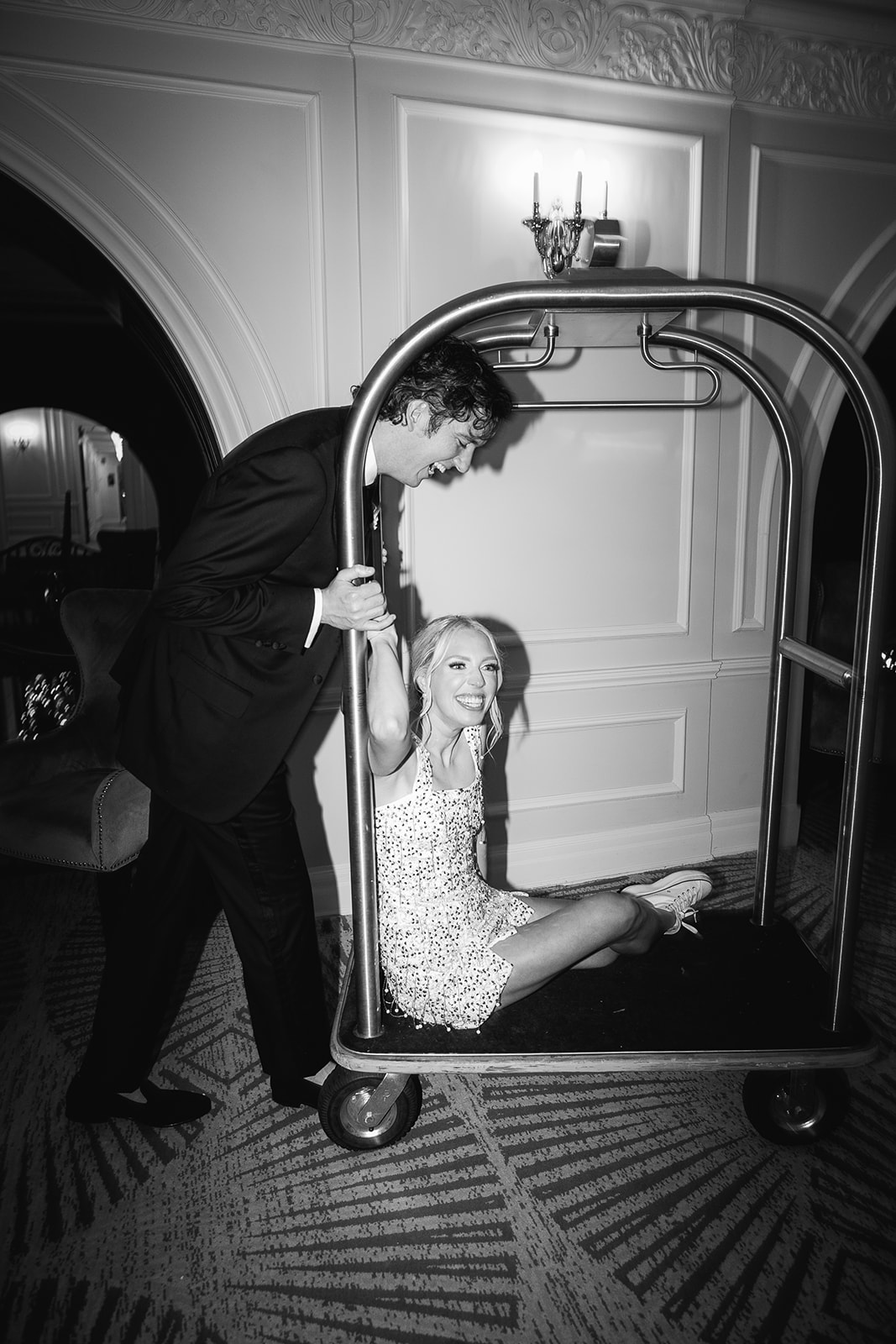 Groom pushes bride on luggage cart inside The Read House wedding venue 