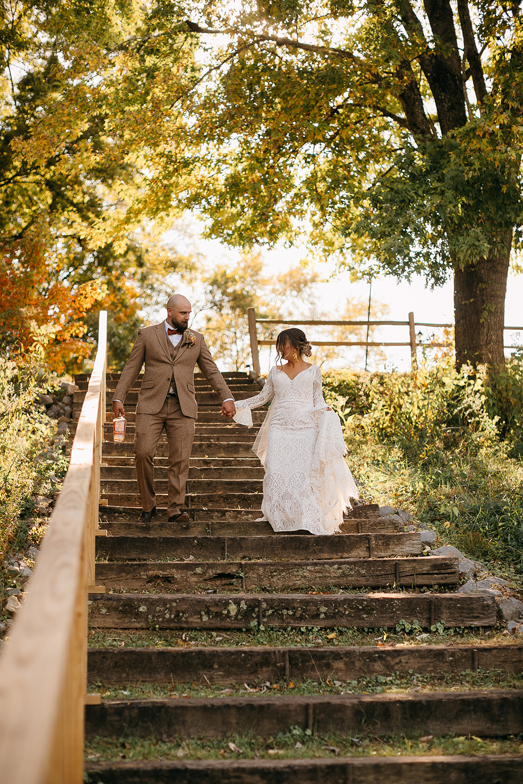 Bride and groom walking down rustic steps surrounded by trees at Tennessee River Place wedding venue. 