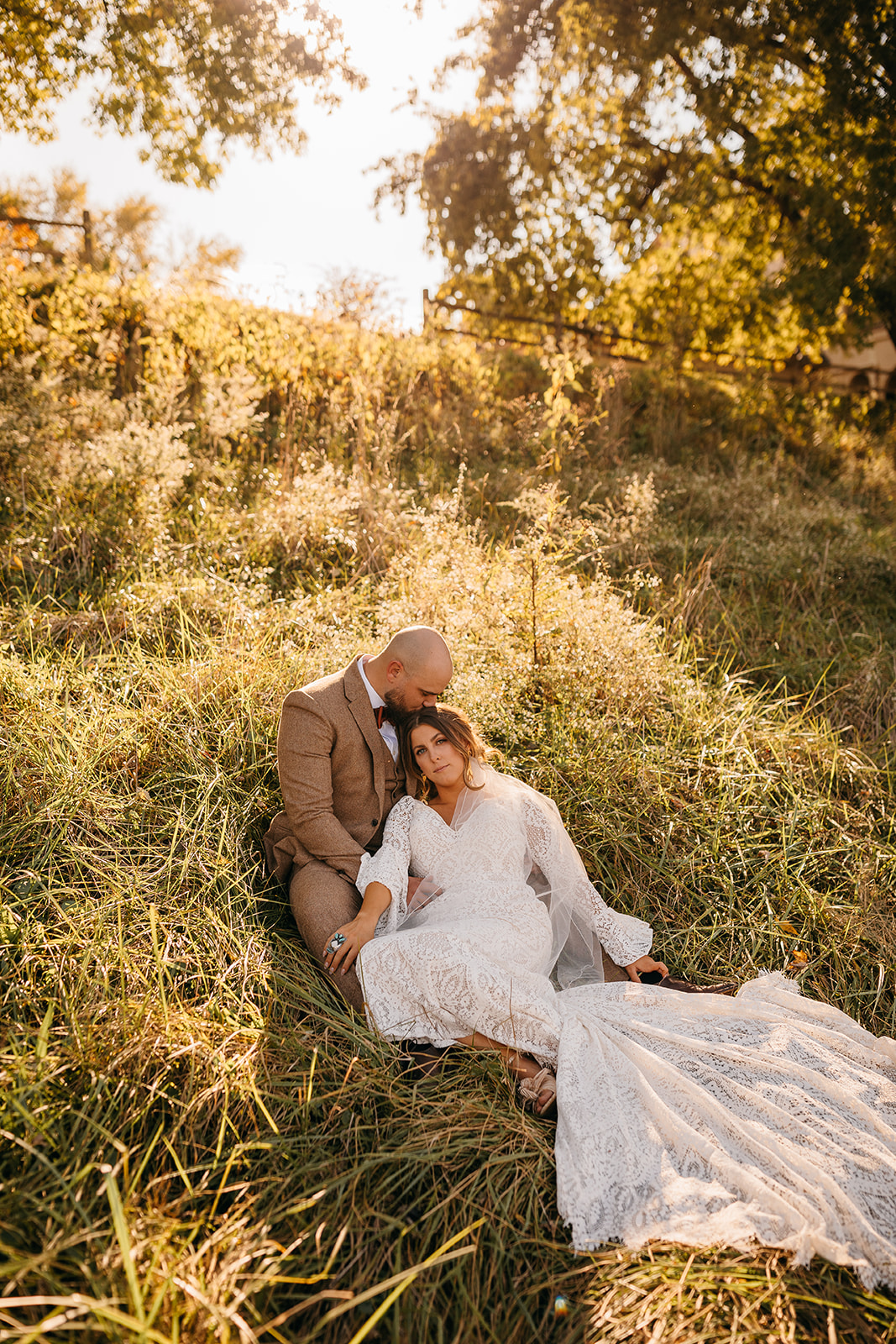 Bride and groom sitting together in tall grass with warm sunlight at Tennessee River Place wedding venue.