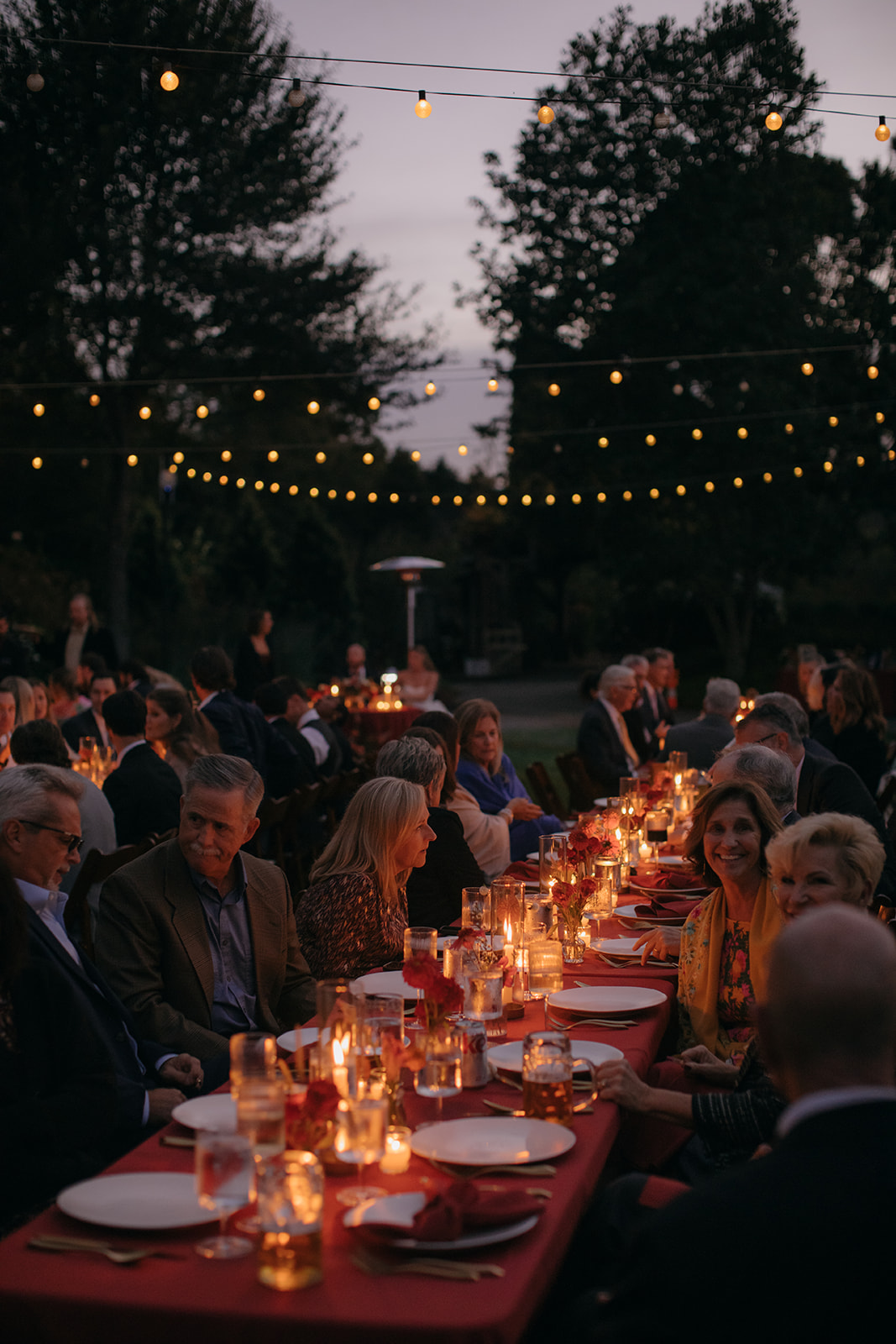 Guests enjoying dinner outdoors beneath string lights at a North Carolina Arboretum wedding reception.