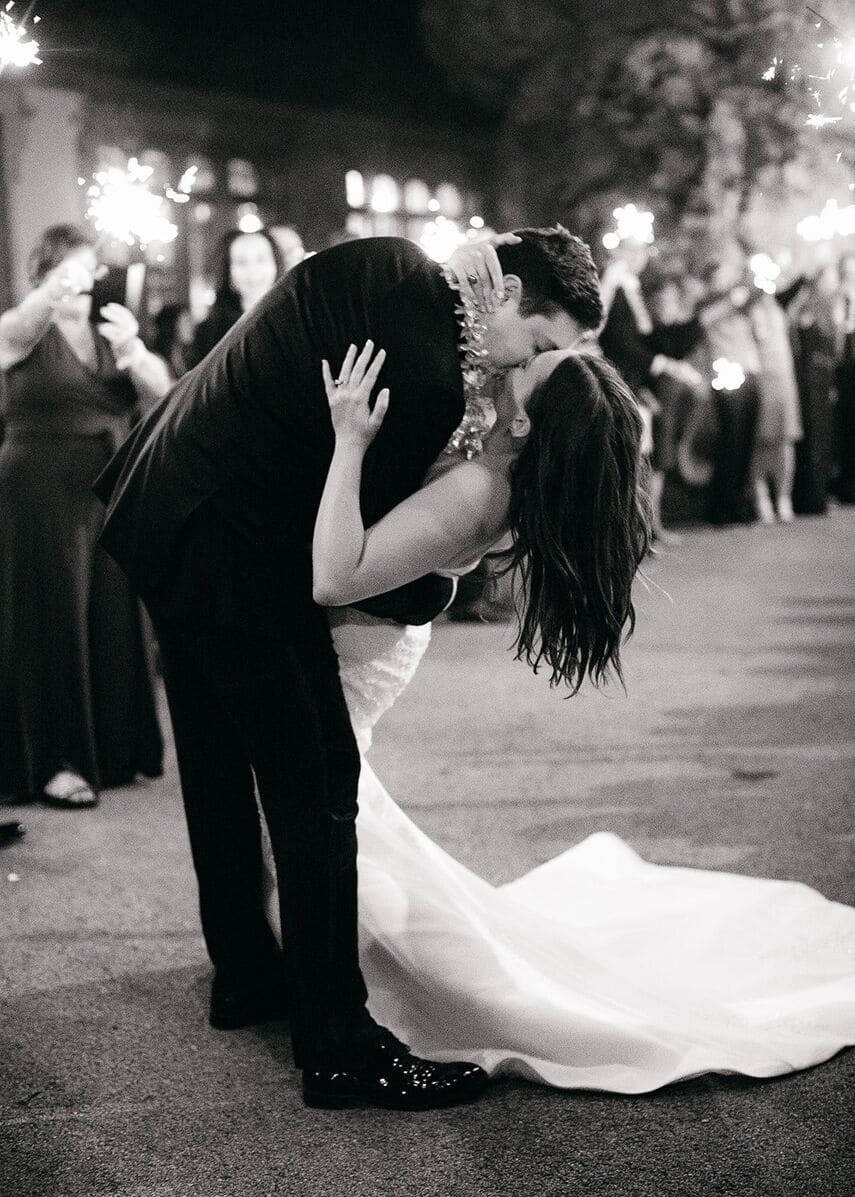 groom dipping bride while guests hold sparklers for their exit
