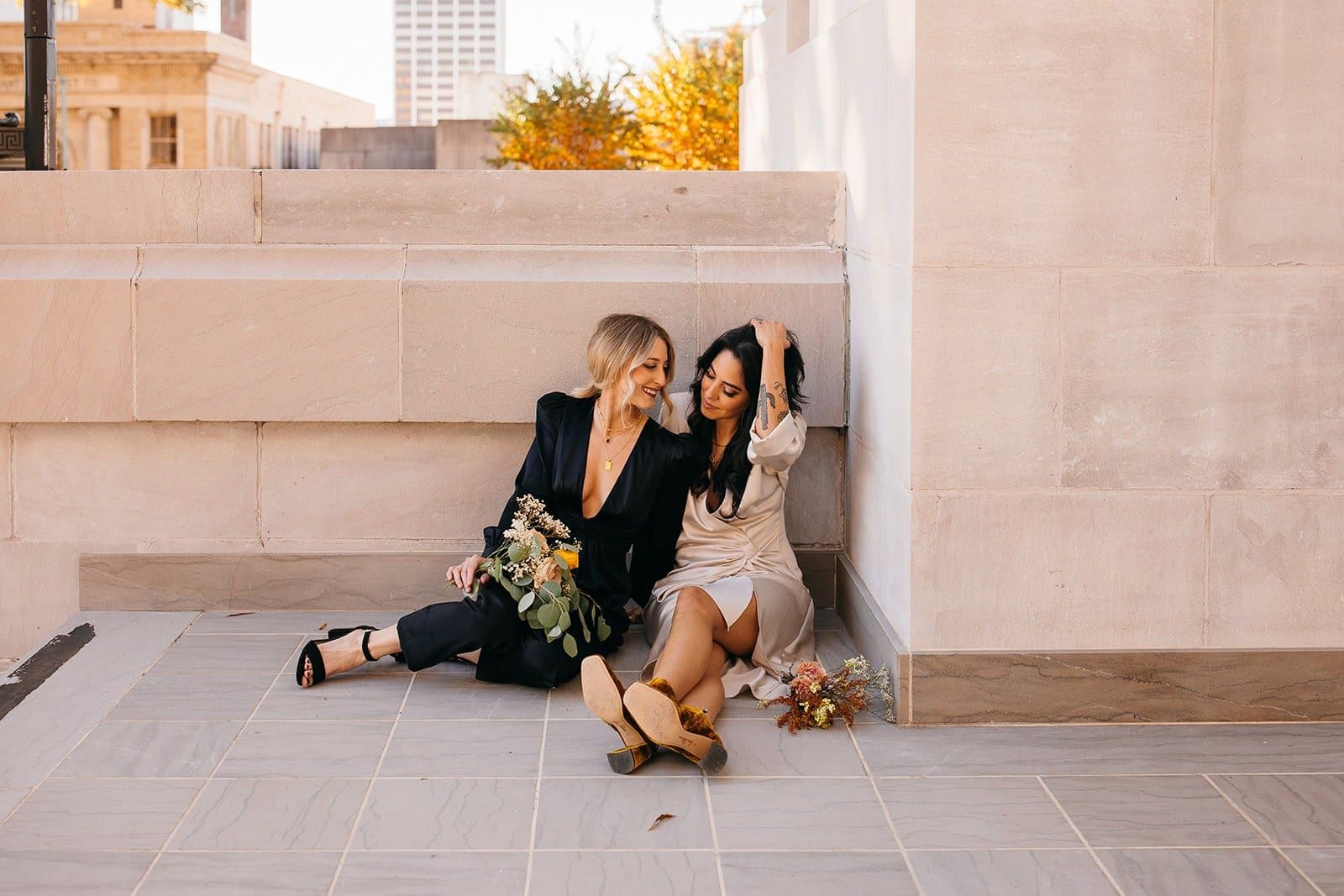 Lesbian couple smiling at one another and sitting on their wedding day