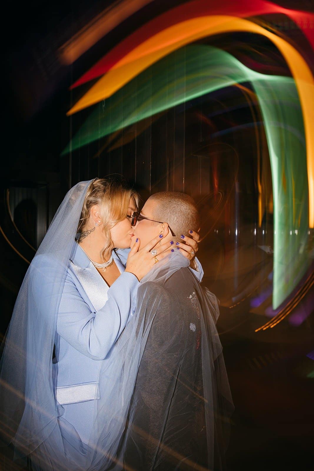 queer couple kissing one another with colorful lights around them